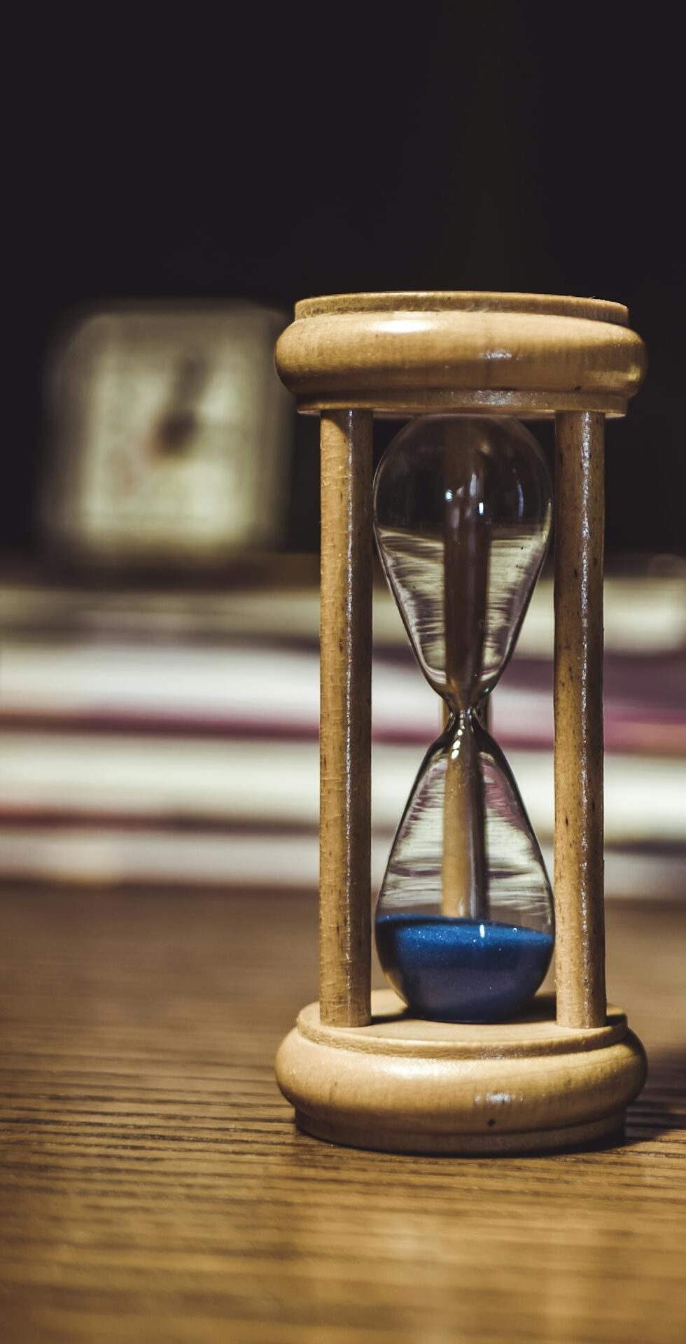 A close-up of a wooden hourglass with blue sand on a wooden desk, symbolizing time and patience.